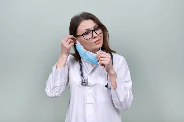 Woman doctor with stethoscope puts on medical protective mask — Stock Photo, Image