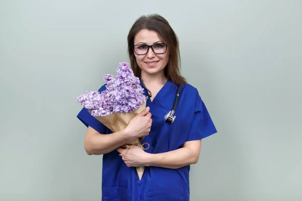 Smiling mature woman doctor nurse with bouquet of flowers