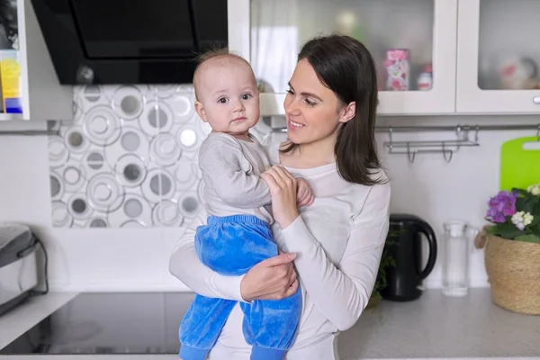 Улыбающаяся женщина держит годовалого ребенка на руках на кухне — стоковое фото