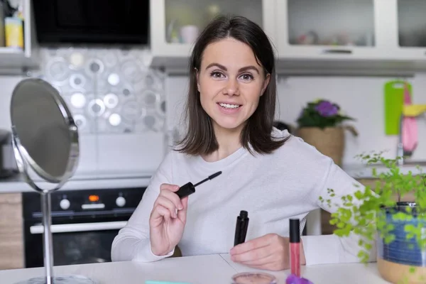 Jonge aantrekkelijke vrouw doet make-up, vrouw zit thuis aan tafel in de keuken met cosmetische — Stockfoto