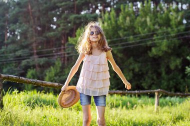 Mutlu kız yaz tatilinin tadını çıkarıyor, yeşil çayırdaki çocuk şapkayla oynuyor.