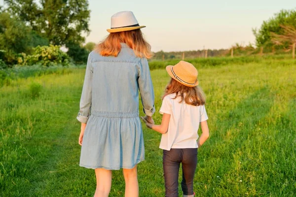 Vista trasera, dos niñas niños van cogidos de la mano en un prado verde de verano — Foto de Stock