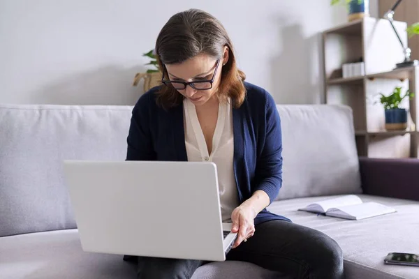 Dojrzałe kobieta pracuje zdalnie w domu, biznes kobieta freelancer siedzi na kanapie z laptopem — Zdjęcie stockowe