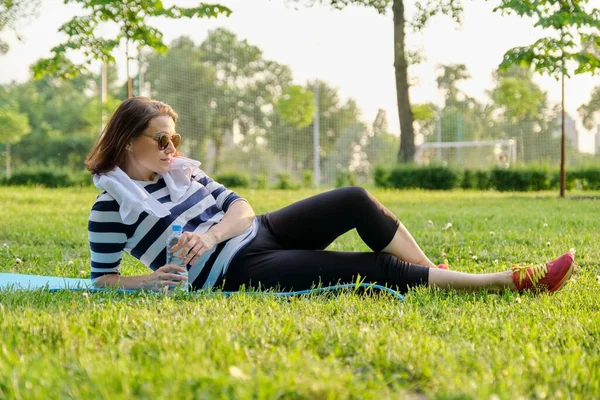 Mujer madura descansando después de ejercicios de ajuste en la estera en el parque — Foto de Stock
