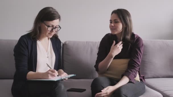 Ung kvinna i samråd med psykolog. Kvinnlig patient som sitter på soffan och pratar om psykiska problem. — Stockvideo