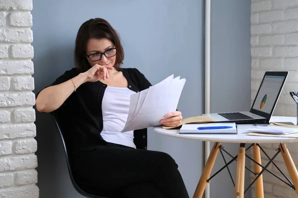 Dojrzała kobieta pracuje w biurze domowym, kobieta siedzi przy biurku z laptopem — Zdjęcie stockowe