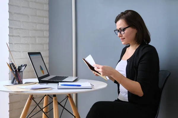 Зріла бізнес-леді з паперовим конвертом сидить за столом з ноутбуком — стокове фото