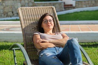 Yetişkin bir kadın çimenlikteki bir sandalyede dinleniyor.