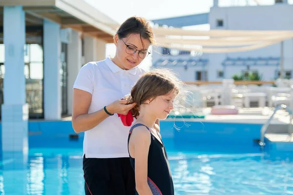 Mamá ayuda a su hija a usar gorra de natación, fondo de piscina al aire libre — Foto de Stock