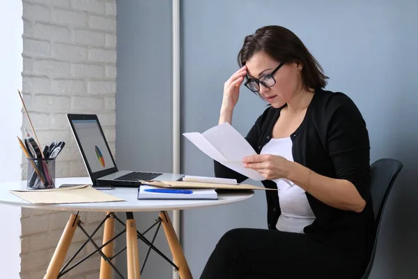 Zdenerwowany smutny w średnim wieku kobieta z papieru laptop siedzi w domu przy stole — Zdjęcie stockowe