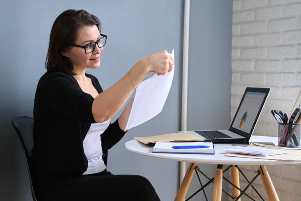 Зріла жінка працює в домашньому офісі, жінка сидить за столом з ноутбуком — стокове фото