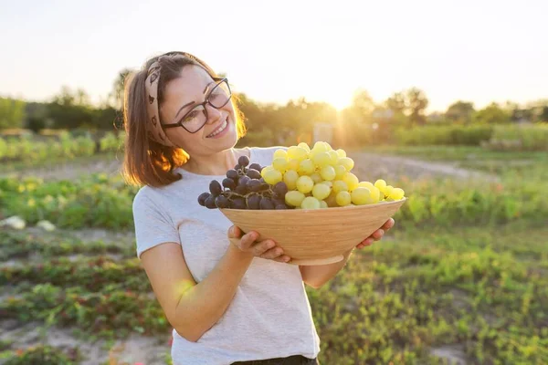 Vrouw met schaal van vers geplukte blauwe en groene druiven, zonnige tuin achtergrond — Stockfoto