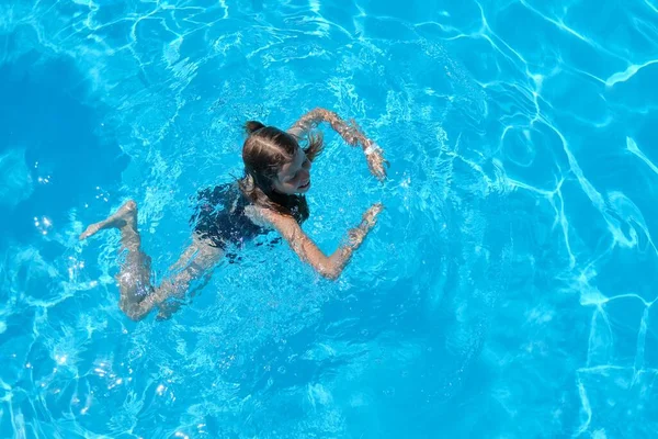 Kid heeft plezier in een buitenzwembad, kind meisje zwemt, duiken, speelt op het water, blauwe achtergrond — Stockfoto