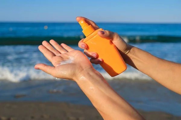 Primer plano de la mujer que aplica loción bronceadora, arena playa fondo azul mar — Foto de Stock