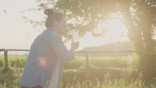 Femme versant de l'eau minérale de la bouteille dans du verre, femme buvant de l'eau claire avec plaisir, coucher de soleil soleil nature fond — Video