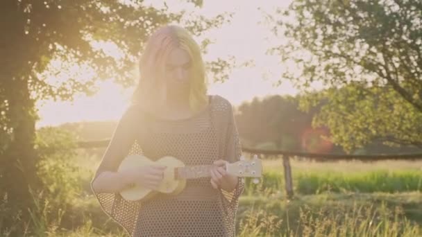 Adolescente chica juega en ukelele, hipster con el pelo teñido de color descansando sentado en la hierba con la guitarra hawaii — Vídeos de Stock