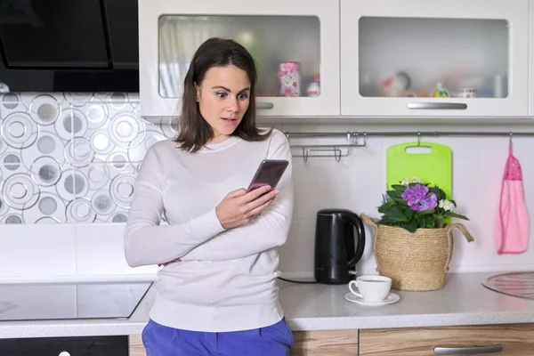 Молода жінка використовує смартфон, домашній кухонний інтер'єр фону — стокове фото