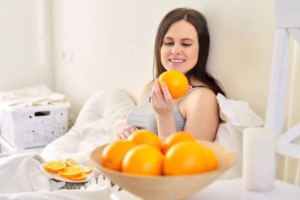 Jovem mulher grávida bonita com laranjas, em casa sentado na cama — Fotografia de Stock