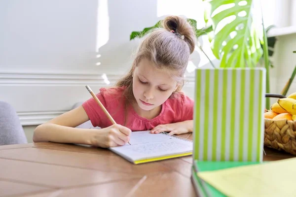 Дівчинка навчається вдома, сидячи за столом — стокове фото
