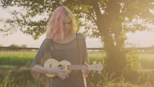 Tonårstjej spelar på ukulele, hipster med färgat färgat hår vilar på gräs med hawaii gitarr — Stockvideo