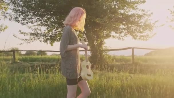 Vacances d'été, heureuse adolescente marchant sur la route de campagne avec guitare ukulélé, hipster à la mode avec cheveux teints aime le week-end et la nature, fond de campagne — Video