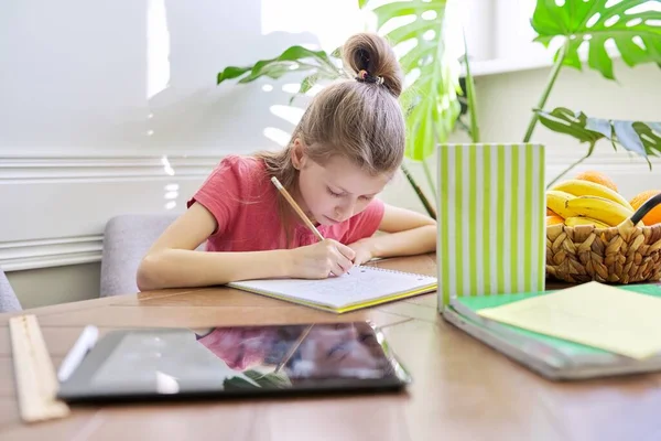 Дівчинка навчається вдома, сидячи за столом — стокове фото