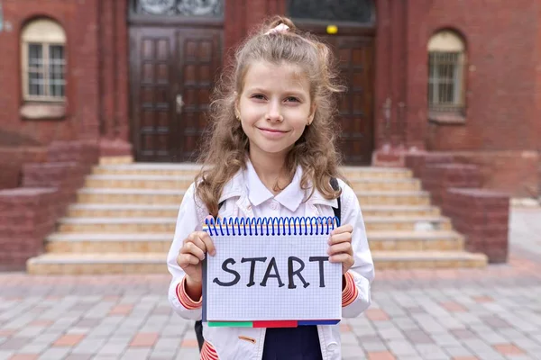 Uczennica szkoły podstawowej z notatnikiem i ręcznie napisane słowo start — Zdjęcie stockowe