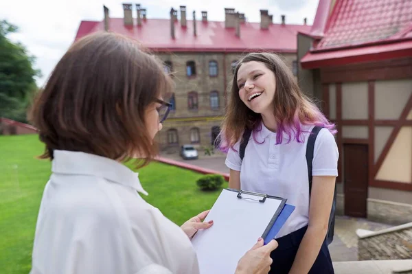 Tiener student meisje praten met leraar, vrouw met klembord — Stockfoto