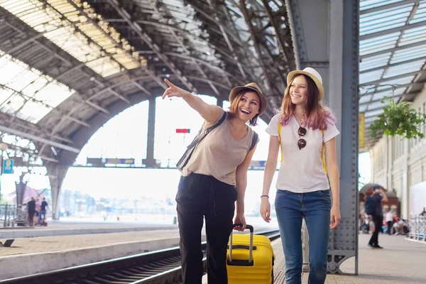 Счастливая мать и дочь-подросток гуляют с чемоданом на вокзале — стоковое фото