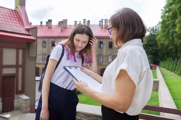 Tiener student meisje praten met leraar, vrouw met klembord — Stockfoto