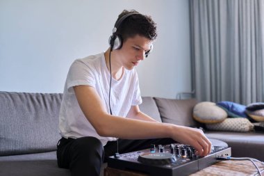 Mikser ekipmanları ile DJ istasyonunda kulaklık takan yaratıcı genç çocuk.