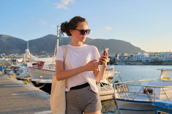 Güzel genç kız rıhtımda rıhtımlı yatlarla, akıllı telefonlu ergenlerle yürüyor. — Stok fotoğraf