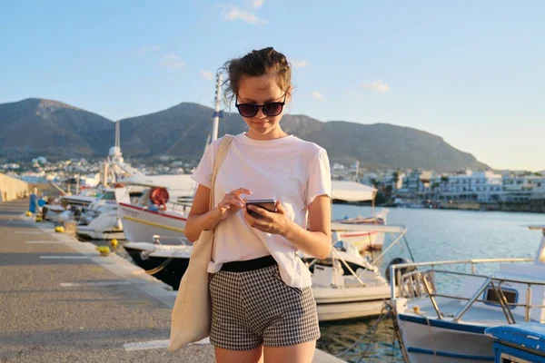 Piękna nastolatka spaceru wzdłuż molo morze z dokowane jachty, nastolatek ze smartfonem — Zdjęcie stockowe