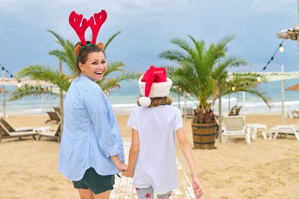 Χαρούμενη μαμά και κόρη παιδί σε Σάντα καπέλο με τα πόδια κατά μήκος της παραλίας, πίσω όψη — Φωτογραφία Αρχείου