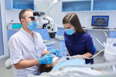 Erkek doktor dişlerini diş mikroskobu aletleriyle tedavi ediyor.