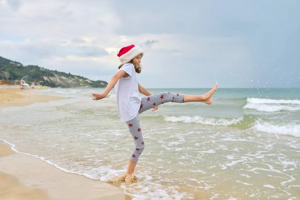 Ιστορικό θάλασσα ωκεανό παραλία, κορίτσι παιδί σε Σάντα καπέλο έχοντας διασκέδαση, πίσω όψη — Φωτογραφία Αρχείου