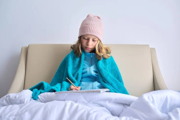 Temporada fria, menina criança em casa em chapéu de malha sob cobertor quente — Fotografia de Stock