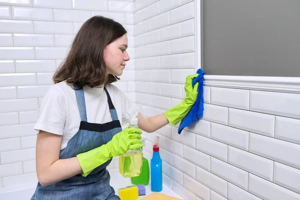 Holka uklízí v koupelně. Teenager v rukavicích zástěry s čisticím prostředkem a hadrem — Stock fotografie