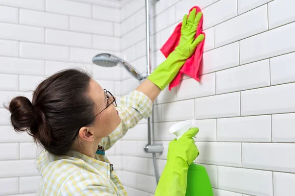 Уборка ванной комнаты, домохозяйка стирает белую плитку стены с моющим средством и тряпкой — стоковое фото