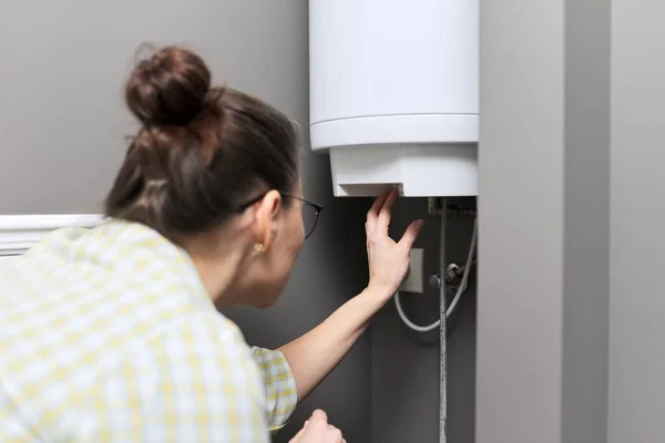 Aquecedor de água em casa, a mulher regula a temperatura em um aquecedor de água elétrica — Fotografia de Stock