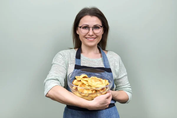 Portrait of middle-aged woman in an apron with bowl of homemade pancakes