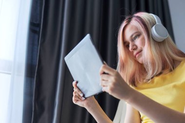 Evde dijital tabletle kulaklık takan liseli kız.