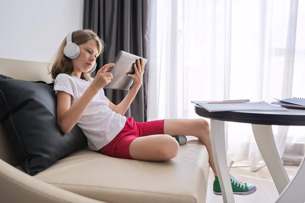 Girl studies online at home, child with digital tablet in headphones