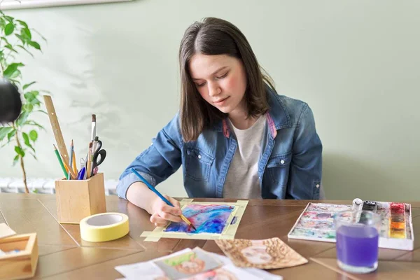 Девушка-подросток рисует акварелью, сидит дома за столом — стоковое фото