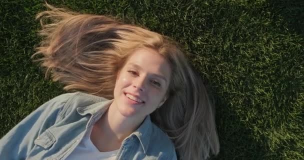 Visão superior do rosto feliz sorridente da jovem mulher bonita deitada na grama verde, dia quente ensolarado — Vídeo de Stock