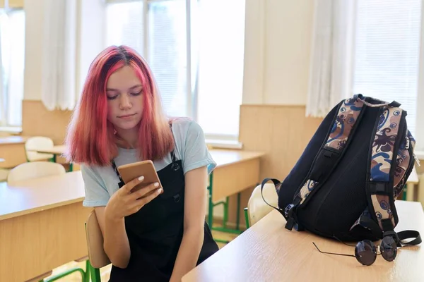 Chica de moda adolescente estudiante de la escuela, en el aula con teléfono inteligente en la mano — Foto de Stock