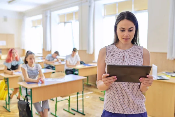 Portret van jonge glimlachende zelfverzekerde vrouwelijke leraar met digitale tablet in de klas — Stockfoto