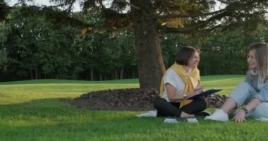 Bayan danışman, çimlerin üzerinde çimlerin üzerinde oturan genç kız öğrenciyle konuşuyor.