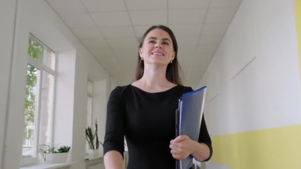 Mujer feliz maestra caminando por el pasillo escolar mirando hacia adelante — Vídeo de stock