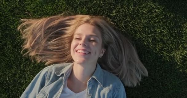 Vista superior de la cara feliz sonriente de la joven hermosa mujer acostada sobre hierba verde, día cálido y soleado — Vídeo de stock